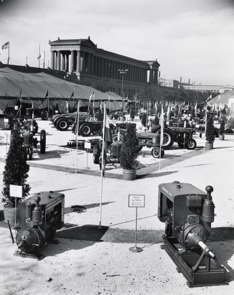 Elevated view of various power units and tractors on display at Soldier Field for International Harvester "100 Years in Chicago" celebration. Original caption reads: "Two International Power Units, the UD-9 Diesel, left, and the new UD-14A Diesel, right, are shown in the foreground of this outdoor machine display at International Harvester's '100 Years in Chicago' exhibition. The power units are part of Harvester's complete line of stationary engines for industrial use. At left, background, is a portion of the 'Progress of Agriculture' tent, in which grain harvesting, cotton picking, modern hay baling, corn picking, beet harvesting, milk production, the Farmall System of Farming, the first Farmall and the millionth Farmall, the 1907 International Auto-Wagon, predecessor to the International Truck, the 1,500,000th International Truck, and 1847 and 1947 kitchens are displayed. Soldier Field's colonnades are in center background. The entire exhibition is on  an 8-acre site at the south end of Soldier Field."