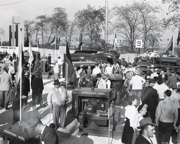 Elevated view of men and women inspecting tractors and engines on display at International Harvester's "100 Years in Chicago" celebration. The exhibition was held at the south end of Soldier Field.
