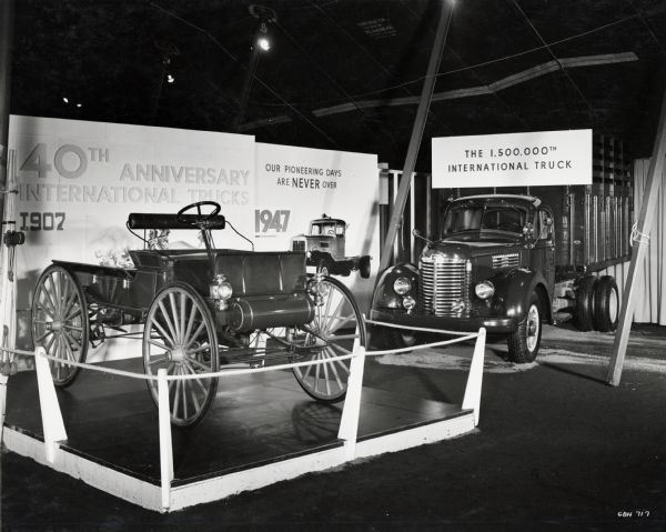 Two International trucks are on display in front of a sign that reads "40th Anniversary International Trucks / 1907" and "Our Pioneering Days are Never Over / 1947." The newer truck is the 1,500,000th International Truck. The display was likely part of the company's "100 Years in Chicago" celebration.