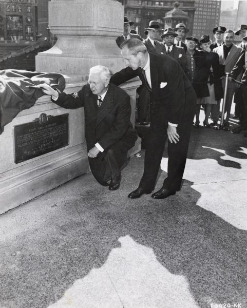 Two men are looking at a newly unveiled plaque commemorating International Harvester's "100 Years in Chicago" celebration. Original caption reads: "Fowler McCormick and Mayor Martin H. Kennelly shown dedicating a plaque commemorating Harvester's 100th Anniversary in Chicago on Michigan Avenue Bridge." Note: The bridge was renamed DuSable Bridge in 2010.