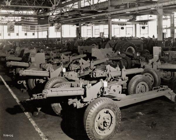 Fifty-seven millimeter artillery pieces stored in an International Harvester factory building. A flag and a poster are hanging from the rafters.