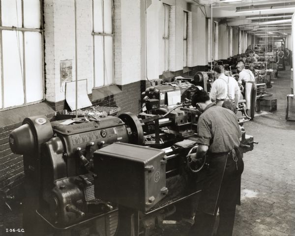 Factory workers machining torpedo parts at an International Harvester factory. Original caption reads: "This section of the torpedo plant houses a line of lathes and grinders used in the machining of torpedo parts."