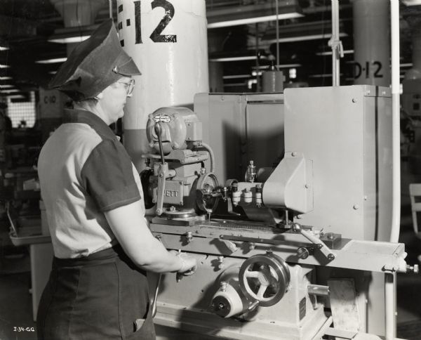 A woman operating a grinding machine at an International Harvester factory responsible for manufacturing aircraft torpedo parts. Original caption reads: "This woman is operating an internal grinder machine, an operation which, because of the skill required has heretofore been regarded as a man's job."