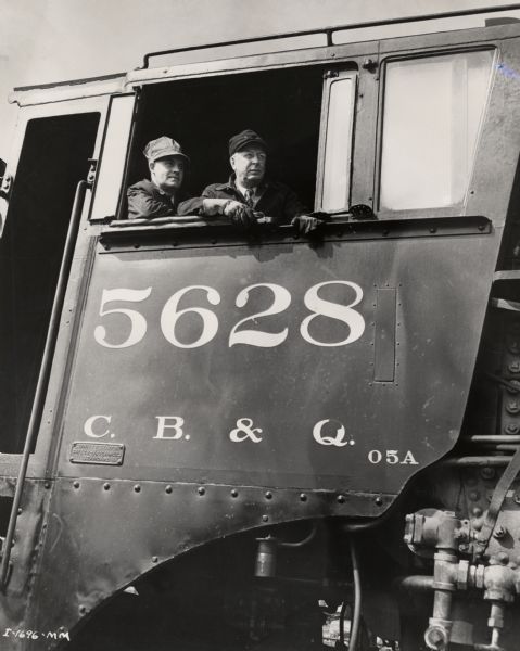 Engineer and fireman on a train carrying International Harvester binder twine ("a trainload of twine") to Lincoln, Nebraska. Original caption reads: "Engineer and fireman of the Harvester twine 'special' assume a striking pose as they arrive in Lincoln. They are F.E. Reishus and F.J. Bjorson, International Harvester district manager and assistant district manager at Lincoln, respectively."