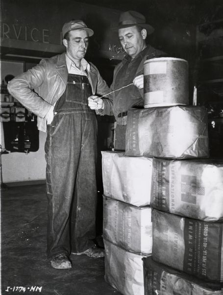 Two men inspect a small piece of binder twine. In front of them are  packaged rolls of International Harvester twine. The men are likely at a dealership or branch house in Lincoln, Nebraska, taking part in a promotion called "trainload of twine."