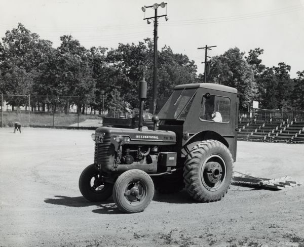 Man grooming a baseball diamond at a community park using an International I-4 tractor. Original caption reads: "International tractor, I-4, used with homemade earth drag. This unit is used to recondition playgrounds. The time required for the average diamond is from 30 to 35 minutes. This one unit is used to keep eleven playgrounds in excellent condition."