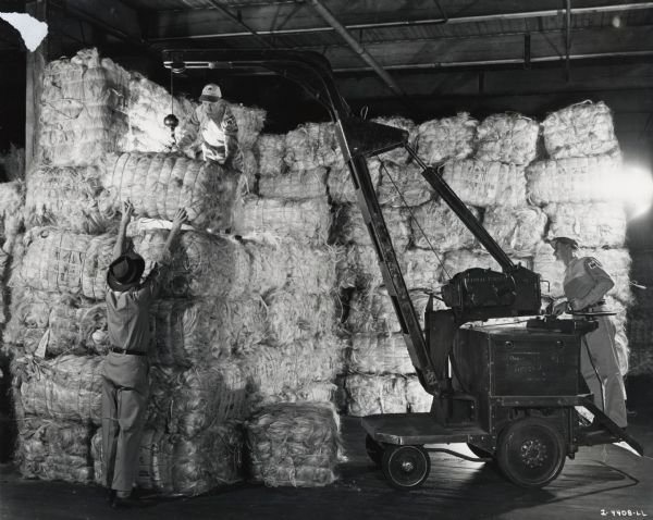 Three men stack bales of sisal fiber. Original caption reads: "Storing the Sisal fiber at the McCormick Twine Mill."