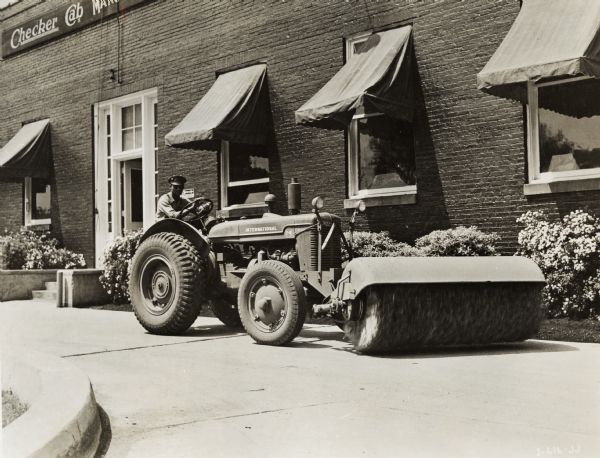 Man with an International I-4 tractor with a Hough front-end broom (street cleaner). A building in the background bears a sign reading: "Checker Cab".
