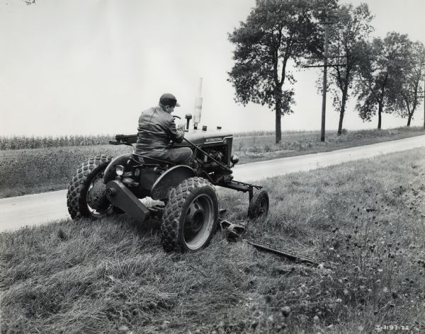 Man mowing the shoulder of a highway or country road with an International A tractor. Original caption reads: "International A industrial wheel tractor with heavy duty AI mower."