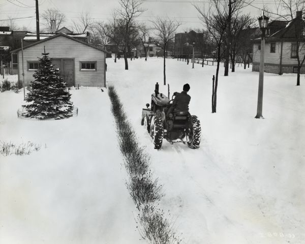 Man using an International A tractor to plow a street. Original caption reads: "The Village of Forest Park, Illinois uses this International A tractor and Myers snow plow to keep its 28 miles of sidewalks clear of snow. The International A and plow can clear 16 miles per day traveling in high gear (approximately ten mph)." Written above photograph. A man is driving a tractor on a sidewalk near a garage, with homes and other buildings nearby. Pedestrians are crossing the street in the background.