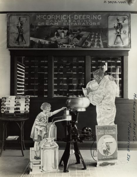 Cream separator advertising display, featuring life-size cutouts of a man pouring milk from a canister and a little girl holding a doll. A sign overhead advertises: "McCormick-Deering Ball-Bearing Cream Separators 'For One Cow or a Hundred'." The display is in the showroom of the Muscatine Implement Company, an International Harvester dealership. There is also a literature rack and bins for spare parts.