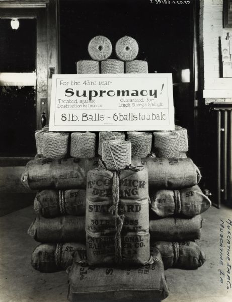 Binder twine display in the showroom of the Muscatine Implement Company, an International Harvester dealership. The display features balls of twine stacked together with a sign reading: "For the 43rd year / Supremacy! / Treated against Destruction by Insects / Guaranteed for Length, Strength & Weight / 8lb. Balls-6 balls to a bale."