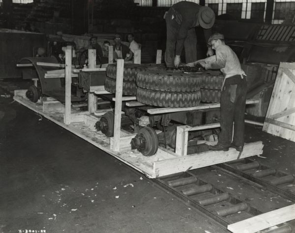 Factory workers packing M-5-6 trucks into crates, possibly at International Harvester's Ft. Wayne Works. Original caption reads: "The trucks in the assembly line are the military model M-5-6, originally sold to the United States Army. These trucks have been diverted under the Lease-Lend Program to Russia."