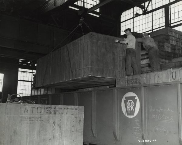 Factory workers move crates containing International M-5-6 trucks onto rail cars, possibly at International Harvester's Ft. Wayne Works. Original caption reads: "The trucks are the military model No. M-5-6, originally sold to the United States Army. These trucks have been diverted under the Lease-Lend Program to Russia."