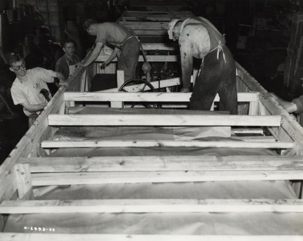 Factory workers packing International M-5-6 trucks into crates, possibly at International Harvester's Ft. Wayne Works. Original caption reads: "The trucks in the assembly line are military model M-5-6, originally sold to the United States Army.  These trucks have been diverted under the Lease-Lend Program to Russia."