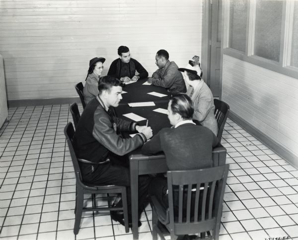 A group of men and women who have applied for employment at the new St. Paul Works sit around a table. They are being interviewed by representatives of International Harvester's Employment Department. The St. Paul Works was set up to produce medium caliber artillery guns for the U.S. Military.
