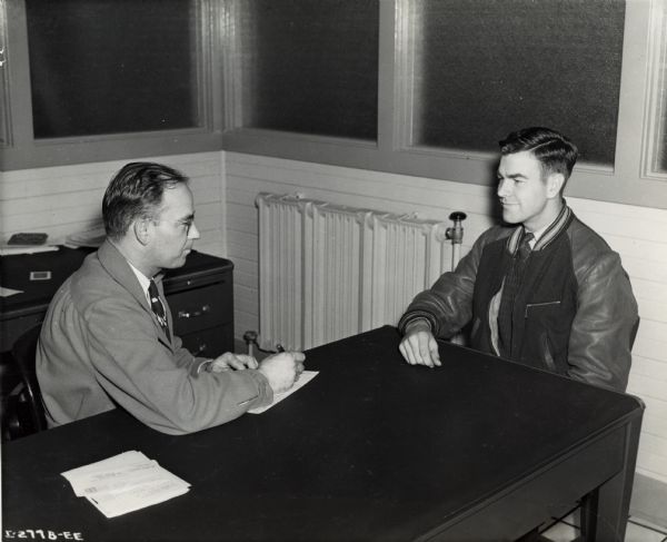 A job applicant interviews at International Harvester's St. Paul Works. Original caption reads: "Medium Caliber Artillery Gun Manufacture. H.E. Palmer, industrial relations manager of the St. Paul gun plant, interviews an applicant for employment preparatory to the beginning of manufacture on the government contract."