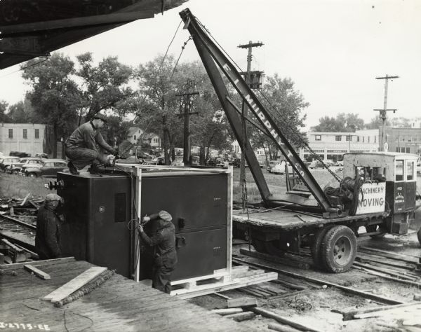 Factory workers use a crane mounted on a truck to unload a transformer on the loading dock of International Harvester's St. Paul Works. Original caption reads: "Medium Caliber Artillery Gun Manufacture. A vast amount of machinery had to be assembled to put the plant in operation in the shortest possible time.  Here a part of a transformer is moved into the plant for the plant's electric power system."