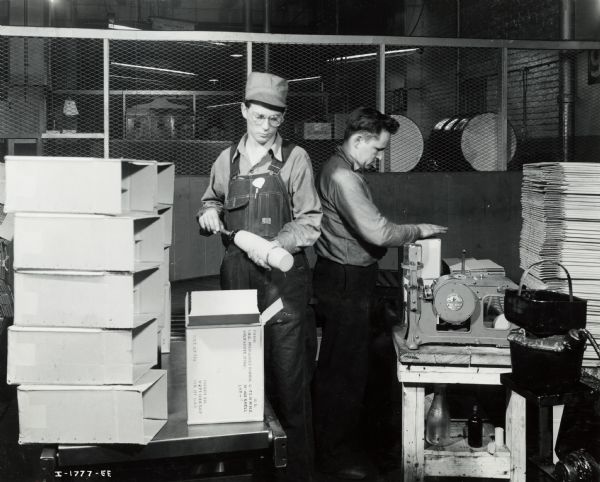Factory workers pack artillery shells into boxes at International Harvester's Milwaukee Works. Original caption reads: "75-Millimeter Shell Manufacture. After the shells have left the painting line they are packed in cartons, [sic] to the carton. Each shell is placed in a separate compartment within the carton to avoid jostling in shipping."