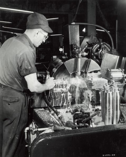 Factory worker producing artillery shells at International Harvester's Milwaukee Works. Original caption reads: "75-Millimeter Shell Manufacture. In another operation on a Gisholt automatic lathe the base of the shell is faced to the proper length and grooved. In the same operation the base for the copper band, affixed later, is turn crimped."