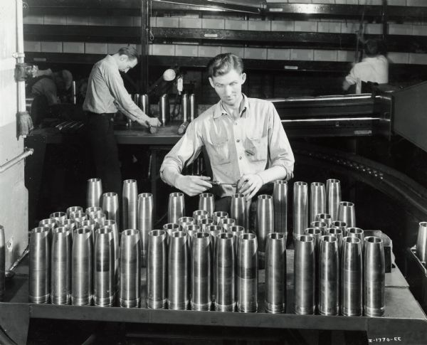 Factory workers producing artillery shells at International Harvester's Milwaukee Works. Original caption reads: "75-Millimeter Shell Manufacture. A set screw is placed in the shell preparatory to painting."