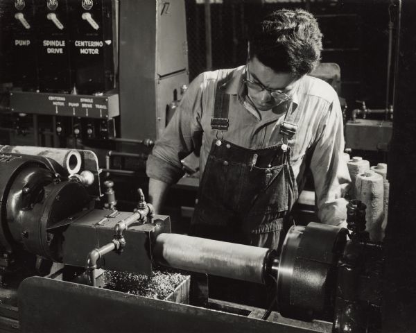 Factory workers producing artillery shells at International Harvester's Milwaukee Works. Original caption reads: "75-Millimeter Shell Manufacture. The first operation in the machining department consists of the centering of the shell. This is done to assure concentricity. The shell is placed on an expanding mandrel for the centering operation, upon which all succeeding operations on the shell are dependent."