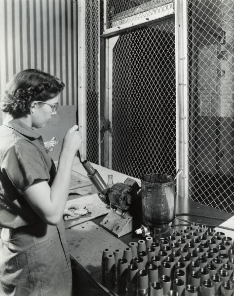 Female factory worker greasing artillery shells at International Harvester's West Pullman Works. Original caption reads: "37-Millimeter Shell Manufacture. Following the painting, the nose threads of the shell are greased preparatory to packing."