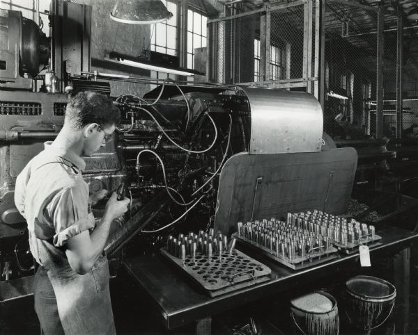 Factory worker producing artillery shells at International Harvester's West Pullman Works. Original caption reads: "37-Millimeter Shell Manufacture. The six-spindle automatic screw machine which roughs and finishes on the outside, threads the nose end and knurls the exterior to take the copper band. This is the original operation on the 1-5/8 inch bar stock."