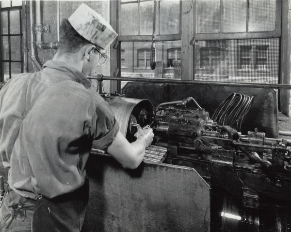 Factory worker producing artillery shells at International Harvester's West Pullman Works. Original caption reads: "37-Millimeter Shell Manufacture. The four-spindle chucking machine which drills, reams, chamfers, and faces the end."
