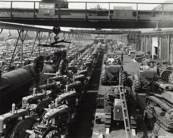 Factory workers loading Farmall tractors onto rail cars outside International Harvester's Tractor Works. Original caption reads: "Machines for use in the peacetime or wartime production of food and military activity. On the long line of flat cars on the left are Farmall tractors destined for food production. Lined up parallel on flat cars at the right is a long line of crawler-type tractors destined for the army to be used in military field operations. Thus is illustrated the dual services of the Harvester Company in this period-production for food and defense."-caption with photograph.

