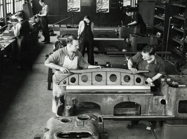 Factory workers rebuilding production machinery at International Harvester's "Special Machine Tool Shop." Original caption reads: "All old machine tools coming into the Harvester Special Machine Tool Shop for rebuilding are torn down completely for repair and checking.  In the section of the plant in this photograph, workman are rebuilding a lathe for one of the manufacturing plants."