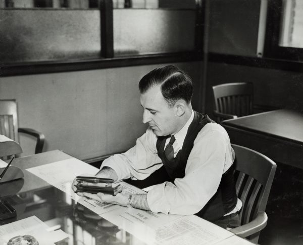 Assistant superintendent of International Harvester's St. Paul Works (factory) examines an artillery shell. Original caption reads: "M.V. Keeler, assistant superintendent, examining a 20 mm shell returned from the gun firing range and converted into a paperweight. The length of the shell is 7-1/4 inches, the length of the projectile three inches."