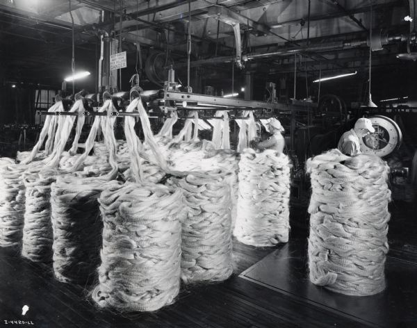 Workers inspect piles of sisal fiber, possibly at the McCormick Twine Mill. Original caption reads: "The piles of fiber shown have been treated with oil, insect and rodent repellents, and fungicide. Each pile of the sliver must conform to specified weight. Operator in the background is splicing fiber for entry into the machine known as the set machine."