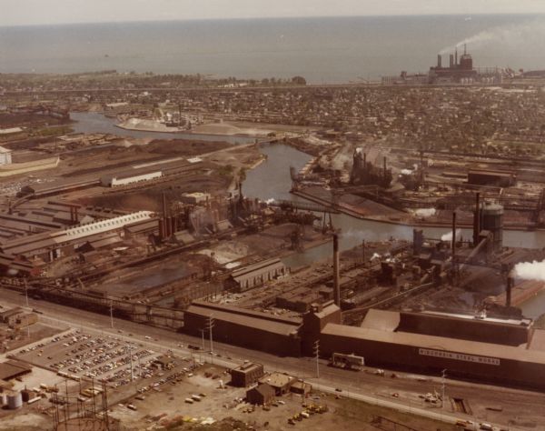 Aerial view of International Harvester's Wisconsin Steel Works, with a river and Lake Michigan in the background.