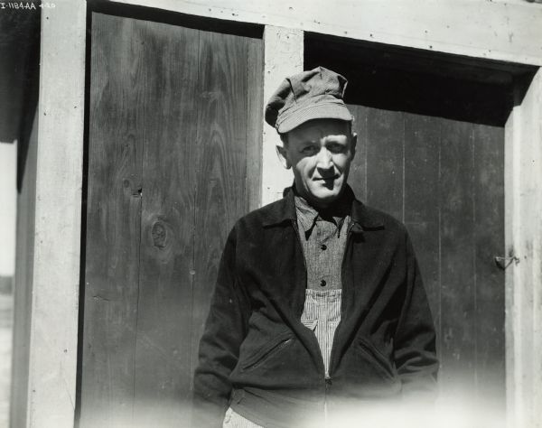 Fred Esser stands in a hat and sweater in front of wooden doors. Mr. Esser owned a McCormick-Deering 6 can cooler.