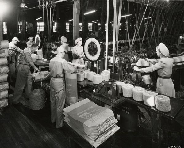 Factory workers weigh and pack binder twine, possibly at the McCormick Twine Mill. Original caption reads: "Weighing, sacking and bale lashing binder twine."