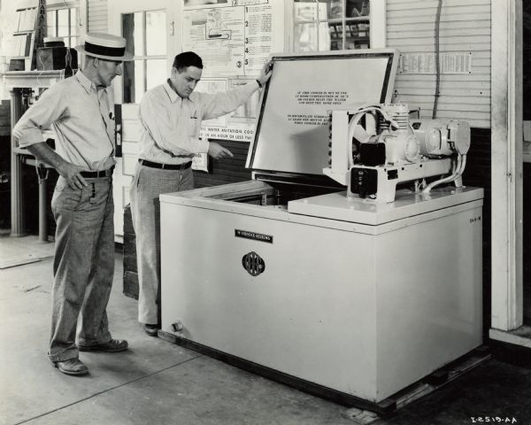 Two men standing next to a McCormick-Deering cooler at Walter & Thompson, an International Harvester dealership. The man pointing to the cooler is P.H. Thompson. The other man is dairyman Logan Hunter.