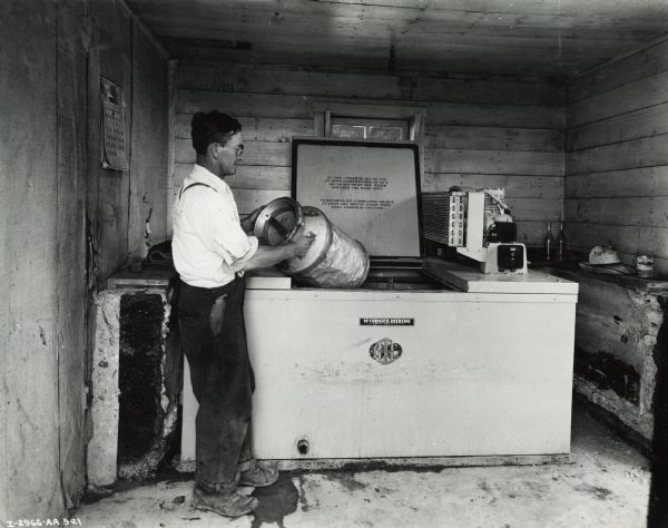 A man is moving a milk can from a cooler in an old building.