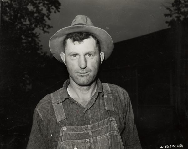 Informal portrait of Edgar Schildknecht, dressed in a hat and overalls. A building is in the background.