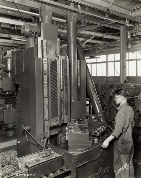Factory worker machining parts at International Harvester's Indianapolis Works.  Original caption states: "Cincinnati Dual-ram Broach for finishing both sides, top of bolt boss, bore of cap, and contact face of cylinder block bearing caps. This improved method of machining assures uniformity of sizes and finishes."