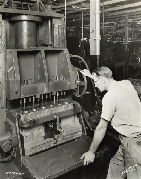 Factory worker at International Harvester's Indianapolis Works.  Original caption states: "American Broach with special index head for pressing in and broaching 12 valve guides simultaneously in the cylinder block."