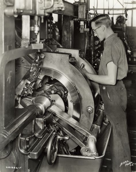 Factory worker at International Harvester's Indianapolis Works.  Original caption states: "LeBlond Crankshaft Lathe showing detail of tool set-up for turning and facing all main bearings simultaneously as well as all diameters on the flange end and pulley end of crankshaft.  This sturdy machine makes it possible to grind main bearings to size directly from this turning operation."