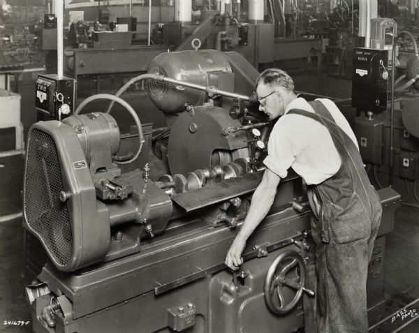 A factory worker wearing safety glasses at International Harvester's Indianapolis Works. Original caption states: "Landis machine for finish grinding main bearings. Note the Arnold Indicator Gauge for sizing work while machine is in operation."