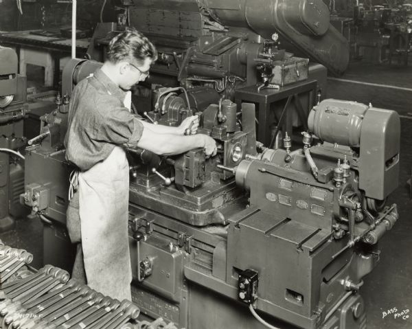 Factory worker at International Harvester's Indianapolis Works.  Original caption states: "One of a group of Excello Precision Boring machines for finish boring both the large and small ends of the connecting rod. This is a double-end machine, and the fixture is hydraulically operated for quick loading and unloading. Fixture and machine assure proper squareness and alignment of wrist pin and crankshaft bores."