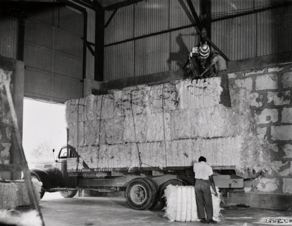 Factory workers loading bales of fiber at an International Harvester sisal plantation in Cuba. Original caption reads: "Loading the weighed bales onto the truck for transporting to railroad cars for reloading onto the sea train."