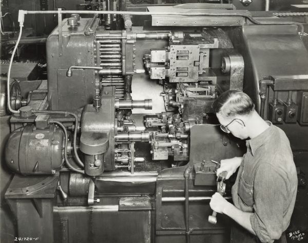 Factory worker with tools at International Harvester's Indianpolis Works. Original caption states: "A special-built Greenlee machine for drilling, reaming, counterboring, and spotfacing the bolt holes in both the connecting rod and cap. A view of the massive index fixture shows various positions in which the rod and cap are held while machining, holding them to tolerances required for International truck engines."