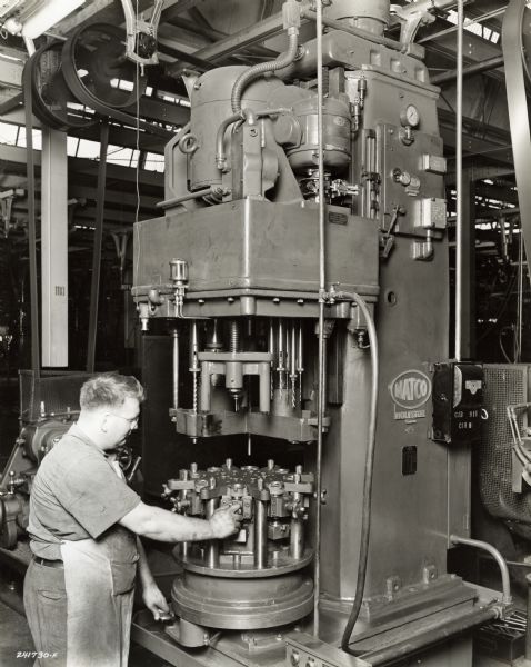 Factory worker with apron at International Harvester's Indianapolis Works. Original caption states: "Natco machine used for drilling all holes, counterboring, reaming, and tapping the oil pump body.  The fixture and the head on the machine are especially built for this operation. The gear shaft hole and the gear diameter are precision bored after this operation to assure perfect alignment."