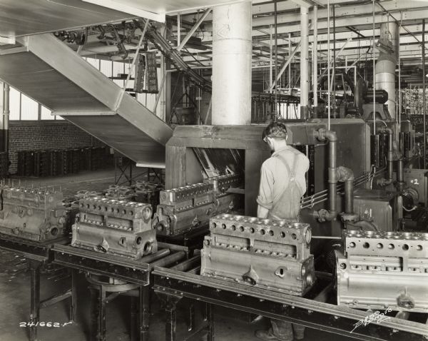 Factory worker at International Harvester's Indianapolis Works (Truck Engine Works). Original caption states: "A Blakeslee washing machine for washing cylinder blocks after all machining operations have been completed. Note the section of overheard conveyor in the background which carries finished parts to the assembly line."