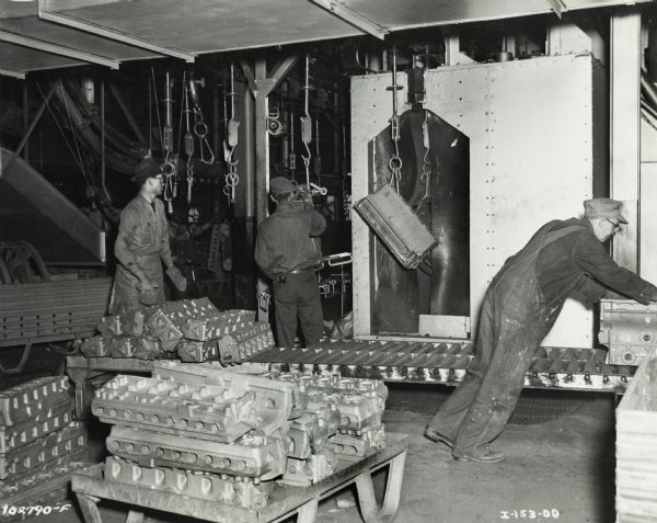 Factory workers at International Harvester's Indianapolis Works (Truck Engine Works). Original caption states: "Castings being taken from Panborn cleaning unit after cleaning operations in which castings are cleaned by the impact of steel shot thrown by centrifugal force."