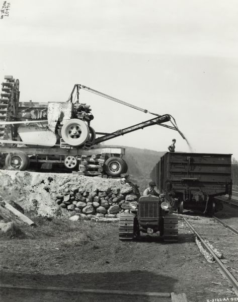 Men load a rail car with crushed gravel or other material using rock crusher(?) on a trailer. The trailer has the text "sold by Dakota Equipment Company, Souix [City, South Dakota?]". One man is operating an Internatioal T-20 TracTracTor (crawler tractor).